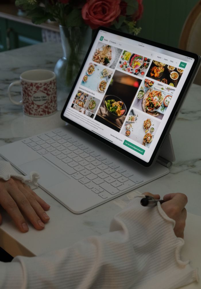 A woman using a tablet to browse meal ideas while sitting at a kitchen table with a coffee mug.
